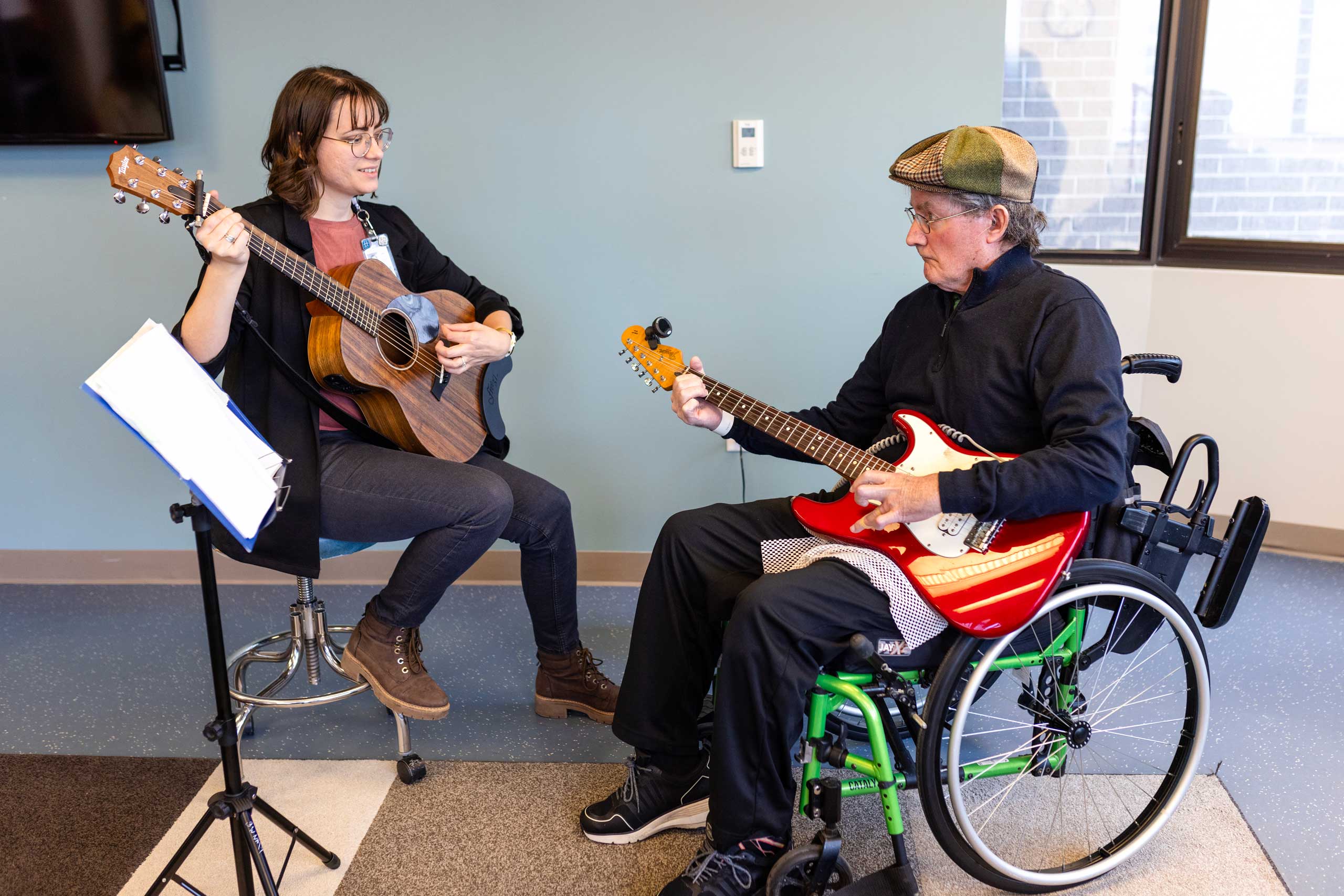 patient  sitting in a wheelchair, re learning how to play guitar with a guitar teacher